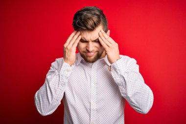 Sarışın, sakallı ve mavi gözlü genç bir işadamı. Kırmızı arka planda zarif bir gömlek giyiyor. Başı ağrıyor çünkü stres altında. Migren ağrısı..