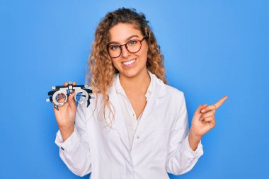 Gözü mavi olan güzel bir kadın izole arka planda optometri gözlüğü tutuyor. Elleri ve parmaklarıyla işaret ederek çok mutlu.