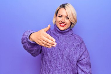 Güzel sarışın ve cüsseli bir kadın mor arka plan üzerine balıkçı yaka kazak giyip dostça gülümseyerek selamlama ve hoş geldin diyor. Başarılı bir iş..