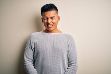 Genç, yakışıklı, günlük kazak giyen, izole edilmiş beyaz arka planda duran, kameraya seksi bir ifadeyle bakan, neşeli ve mutlu yüzlü Latin bir adam..