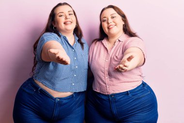 Genç ve cüsseli ikizler günlük kıyafetler giyip neşeli gülümseyerek avuç içi yardım ve kabullenme teklif ediyorlar.. 