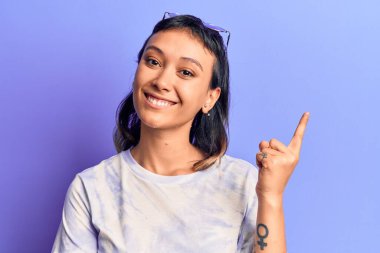 Gündelik kıyafetler giyen genç bir kadın gülümseyerek mutlu bir şekilde elini ve parmağını kenarda gezdiriyor. 