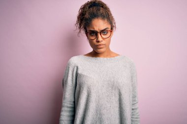 Genç, güzel, Afro-Amerikan kız pembe arka plan kuşkucu ve gergin üzerine süveter ve gözlük takıyor, sorun yüzünden surat asıyor. Negatif kişi.