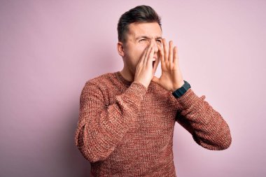 Pembe izole arka plan üzerine sıradan bir kazak giyen yakışıklı beyaz adam elleri ağzında sinirli bir şekilde bağırıyordu.