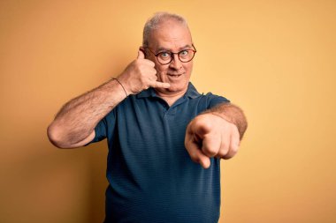 Orta yaşlı yakışıklı beyaz bir adam sarı arka planda güneş gözlüğü takıyor gülümsüyor telefonda konuşuyor ve seni işaret ediyor. Ara beni..