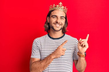 Prens tacı takan yakışıklı genç adam gülümsüyor ve kameraya bakıyor iki eliyle ve parmaklarıyla kenarı işaret ediyor.. 