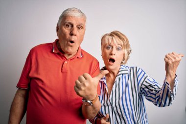 Tecrit edilmiş beyaz arka planda yan yana duran yaşlı ve güzel bir çift. Şaşırmış bir şekilde parmaklarını yana uzatmış, ağzı açık bir şekilde hayret içinde..
