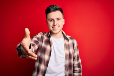 Kırmızı izole edilmiş arka plan üzerine gündelik modern tişört giyen yakışıklı beyaz bir adam gülümseyen bir avuç içi dolusu yardım ve kabullenme sunuyor..