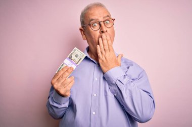 Orta yaşlı, ağarmış bir adam, elinde bir deste banknotla soyutlanmış pembe arka planda, ağzı kapalı, utancından ağzı açık, korku ifadesi, sessizlikten korkan, gizli bir konsept.