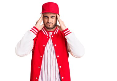 Beyzbol ceketi ve şapkası giyen genç yakışıklı adam baş ağrısı yüzünden çaresiz ve stresli çünkü ağrı ve migren. Eller başının üstünde.. 