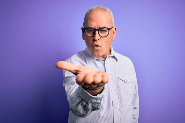 Orta yaşlı, beyaz, çizgili gömlek ve mor arka planda gözlük takan yakışıklı bir adam kameraya bakıp havada öpücükler savuruyor. Güzel ve seksi. Aşk ifadesi.