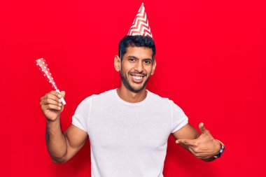 Doğum günü şapkası takan genç Latin adam gülümseyen mutlu ve gururlu birini işaret ediyor. 