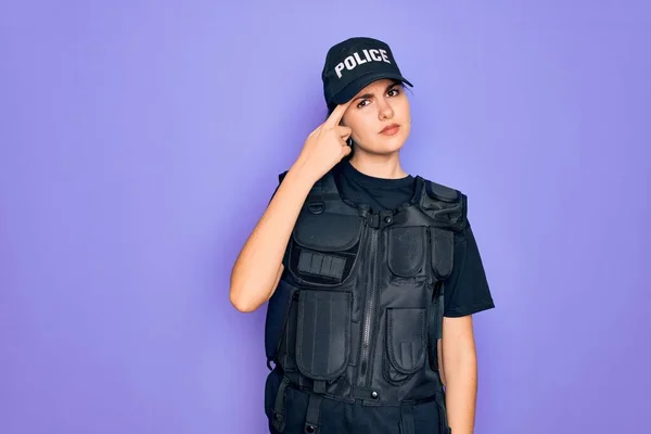 Young police woman wearing security bulletproof vest uniform over purple background pointing unhappy to pimple on forehead, ugly infection of blackhead. Acne and skin problem
