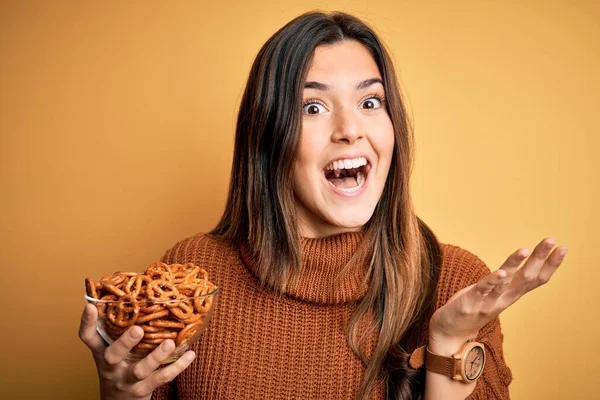 Young Beautiful Girl Eating Baked German Pretzel Standing Isolated Yellow — Stock Photo, Image