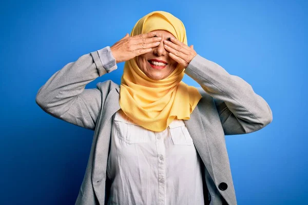 中世のブルネットのビジネス女性は手が陽気で面白い笑顔で目をカバー青い背景にイスラム教徒の伝統的なヒジャーブを身に着けています ブラインドコンセプト — ストック写真