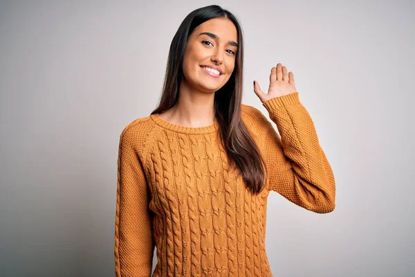 Young beautiful brunette woman wearing casual sweater over isolated white background Waiving saying hello happy and smiling, friendly welcome gesture