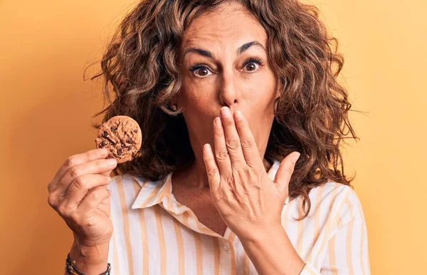 Mulher Morena Meia Idade Segurando Biscoito Chocolate Sobre Fundo Amarelo — Fotografia de Stock