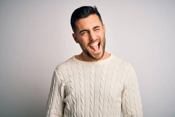 Young handsome man wearing casual sweater standing over isolated white background winking looking at the camera with sexy expression, cheerful and happy face.