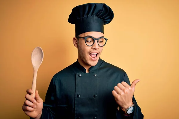 年轻的巴西厨师 身穿炊事服 头戴礼帽 拿着木勺 手指朝外 笑容满面 — 图库照片