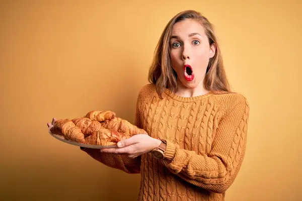 Fiatal Gyönyörű Szőke Kezében Tányér Croissant Felett Elszigetelt Sárga Háttér — Stock Fotó