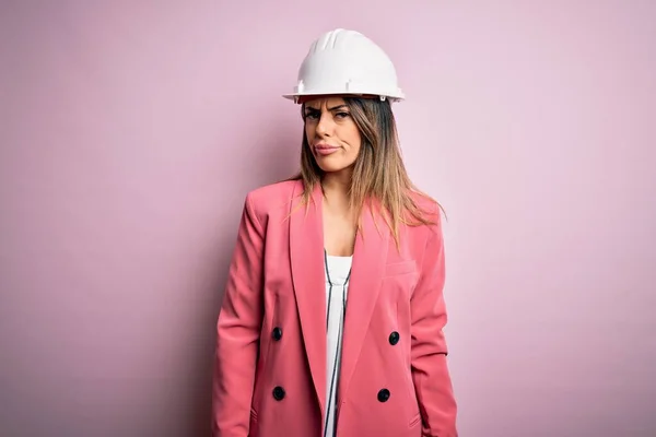 Jonge Mooie Brunette Architect Vrouw Dragen Veiligheidshelm Roze Achtergrond Sceptisch — Stockfoto