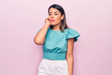 Genç, güzel esmer kadın pembe arka planda duruyor.