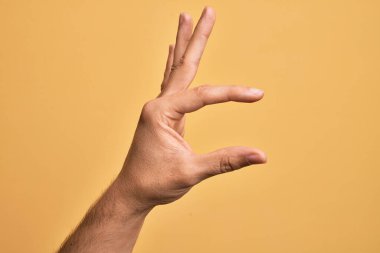 İzole edilmiş sarı arka plan üzerinde parmaklarını gösteren beyaz bir adamın eli. Görünmez bir şeyi alıp, parmaklarıyla uzayı gösteren bir nesneyi tutuyor.