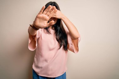 Genç, esmer, zarif bir kadın gözlük takıyor, arka planda izole edilmiş, ellerle gözleri örtüyor ve üzgün ve korku ifadeleriyle dur hareketi yapıyor. Utanç verici ve olumsuz bir kavram..