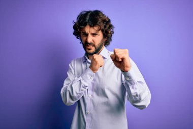 Mor arka plan üzerinde duran sakallı yakışıklı iş adamı yumruk savunma hareketleriyle dövüşmeye hazır sinirli ve üzgün bir yüz, problemden korkuyor.