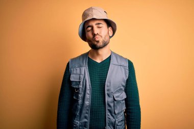 Tatilde sakallı yakışıklı bir turist sarı arka planda kaşif şapkası takıyor ve kameraya bakıp havada öpücük yolluyor güzel ve seksi. Aşk ifadesi.