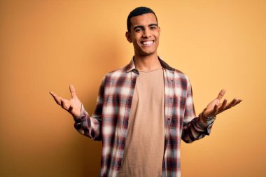 Genç, yakışıklı, Afro-Amerikalı bir adam sarı arka planda dikilmiş neşeli gülümsüyor, dostça karşılıyor, olumlu ve kendinden emin selamlıyor.