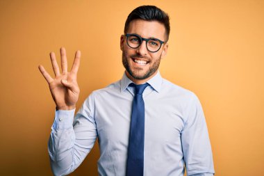 Sarı arka plan üzerinde duran kravat ve gözlük takan genç yakışıklı işadamı dört numaralı parmaklarıyla işaret ederken kendinden emin ve mutlu gülümsüyor..