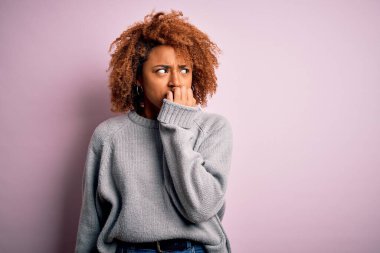 Kıvırcık saçlı, rahat kazak giyen, elleri ağız yiyen, gergin ve gergin bir Afro-Amerikan genç kadın. Endişe sorunu.