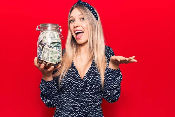 Joven Hermosa Chica Rubia Sosteniendo Tarro Con Ahorros Celebrando Logro —  Fotos de Stock