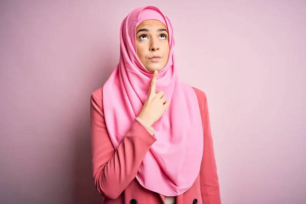 若いです美しいです女の子身に着けていますムスリムヒジャーブ立っています上の隔離されたピンクの背景思考濃縮約疑問について指であごと見上げ疑問 — ストック写真