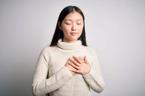胸の上で目を閉じて手で笑顔と顔に感謝のジェスチャー孤立した背景の上に立ってカジュアルなセーターを着て若い美しいアジアの女性 健康コンセプト — ストック写真