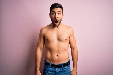 Sakalsız, sakalsız, genç, yakışıklı, güçlü bir adam. Pembe arka planda duruyor. Şaşırmış ve şaşırmış bir ifadeyle, korku ve heyecanlı bir yüzle..