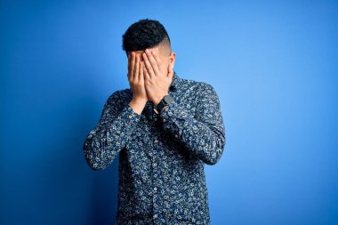 Young handsome man wearing casual shirt standing over isolated blue background with sad expression covering face with hands while crying. Depression concept.