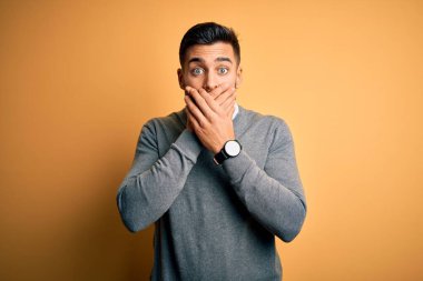 Zarif bir kazak ve sarı arka plan üzerine kravat takan genç yakışıklı işadamı yanlışlıkla ağızlarını kapatarak şok geçirdi. Gizli konsept.