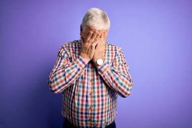 Üst düzey yakışıklı beyaz adam, izole edilmiş mor arka plan üzerine gündelik bir gömlek giyiyor ve ağlarken suratını ellerle kapatıyor. Depresyon kavramı.
