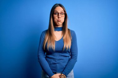 Mavi gözlü, güzel, sarışın, mavi arka planda duran komik yüzlü, güzel bir kadın. Havayla şişmiş ağız, çılgın bir ifade..