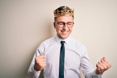 İzole edilmiş arka planda altın taç takan yakışıklı beyaz bir iş adamı. Kolları havada ve gözleri kapalı zaferi kutlarken gülümsüyor. Kazanan konsept.