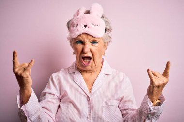 İzole edilmiş pembe arka planda pijama ve uyku maskesi takan son sınıf güzeli bir kadın çılgın bir ifadeyle elleri havada rock sembolü yaparak bağırıyor. Müzik yıldızı. Ağır konsept.