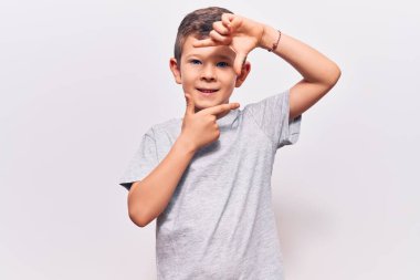 Gündelik kıyafetler giyen sevimli sarışın çocuk gülümseyerek elleri ve parmakları gülen yüzüyle çerçeve yapıyor. yaratıcılık ve fotoğrafçılık kavramı. 