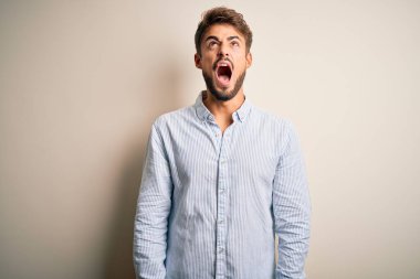 Sakallı, çizgili tişörtlü genç bir adam beyaz arka planda sinirli ve öfkeli bir şekilde bağırıyor. Öfkeyle bağırıyor. Öfke ve agresif kavram.