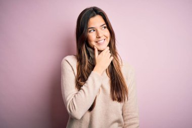 Balıkçı yaka kazak giyen genç ve güzel bir kız. İzole edilmiş pembe arka planda duruyor. Elleri çenesinde, soru sormayı, düşünceli ifadeyi düşünüyor. Düşünceli bir yüzle gülümsüyor. Şüphe kavramı.