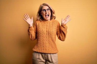 Sarı arka plan üzerine gündelik süveter ve gözlük takmış orta yaşlı güzel bir kadın çılgın ve başarıyı kollarını kaldırıp heyecanla haykırarak kutluyor. Kazanan konsept