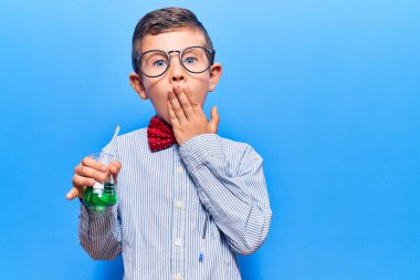 Bilim adamı papyonu takan sevimli sarışın çocuk ve elinde test tüpü ile ağzını kapatmış, şok olmuş ve hata yapmaktan korkan. şaşırmış ifade 