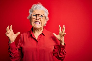 Son sınıf güzeli, gri saçlı, günlük gömlek ve gözlük takan, kırmızı arka planda çılgın, deli deli bağıran, agresif ifade ve kollarıyla bağıran bir kadın. Hayal kırıklığı konsepti.