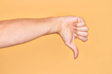 Kafkasyalı genç adam parmaklarını izole edilmiş sarı arka planda gösteriyor. Başparmak hareketi, reddetme hareketi, hoşnutsuzluk ve negatif işaret yapıyor.
